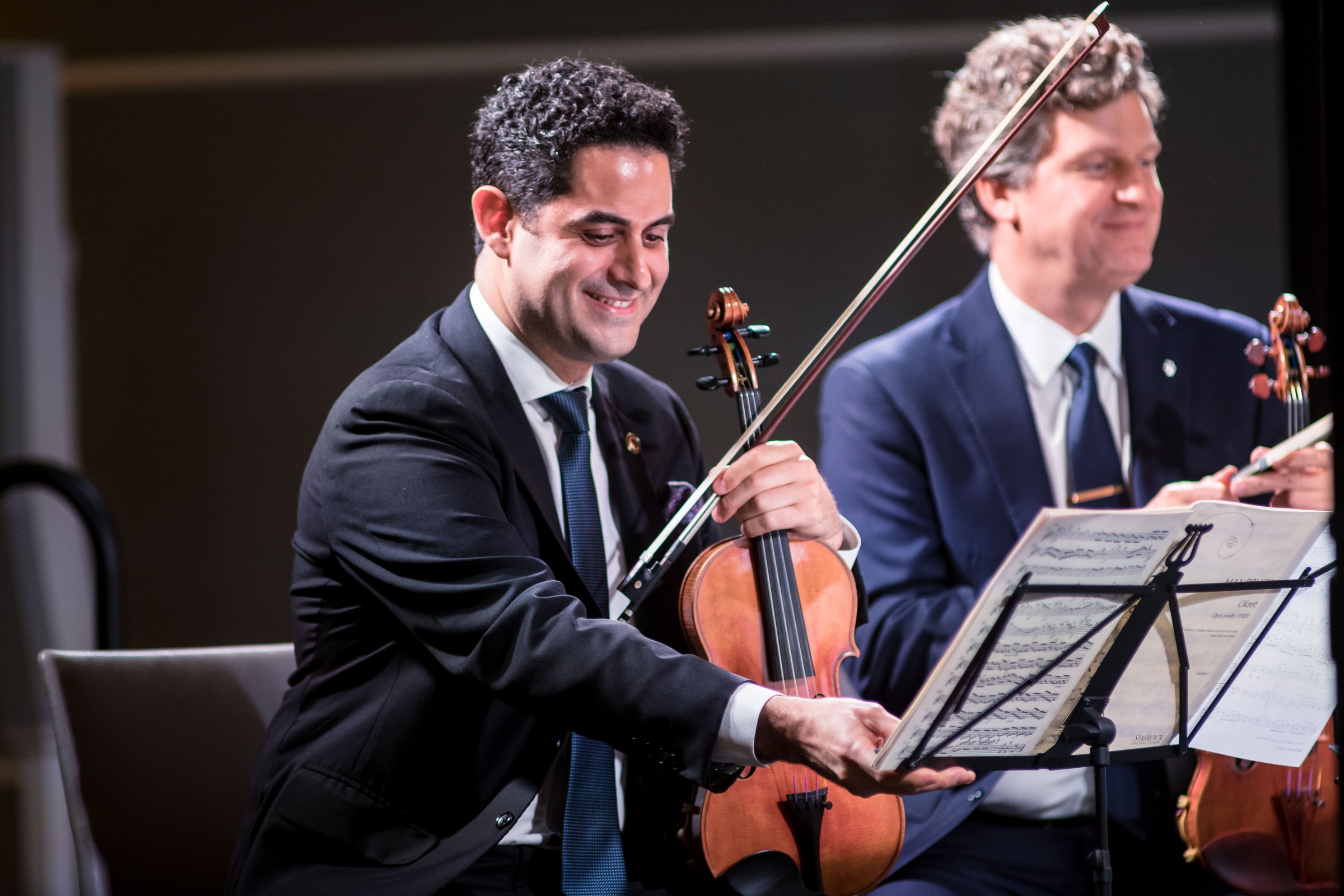 Arnaud Sussmann smiling on stage with his violin beside a colleague.