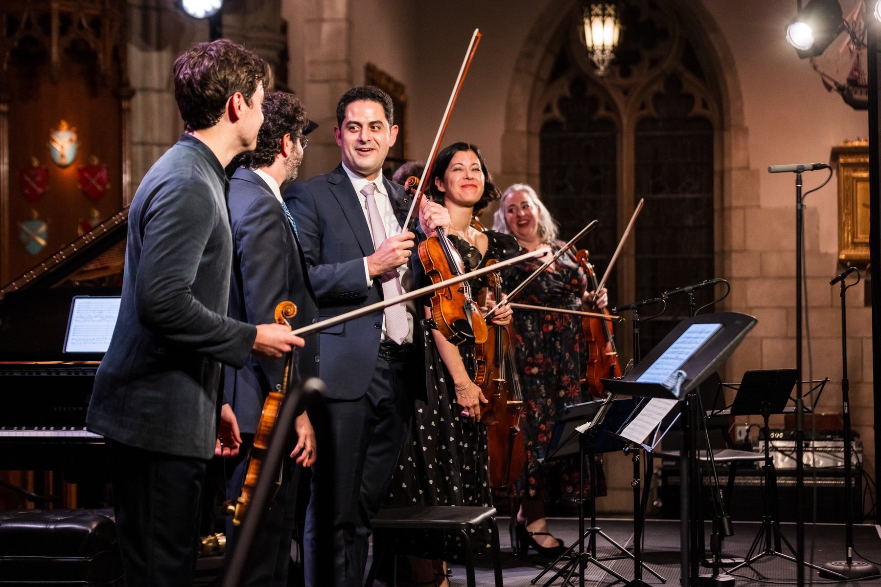 Arnaud Sussmann, violin and bow in hand, smiling with fellow musicians on stage during the applause after Violin Legends, Chamber Music Society of Palm Beach.