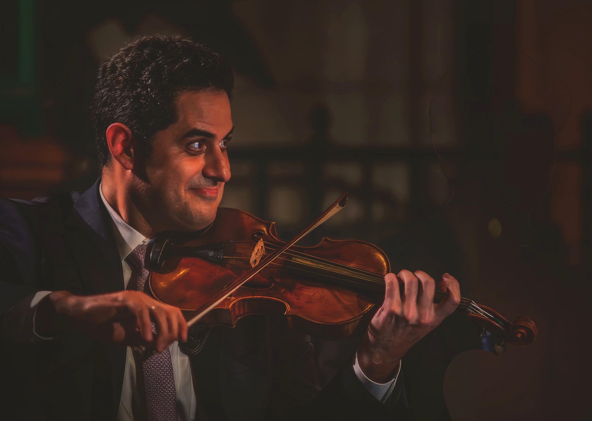 Arnaud Sussmann in concert, dark suit, playing the violin under warm light.